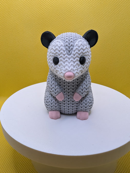 Front view of grey knitted-style opossum with white face and pink paws