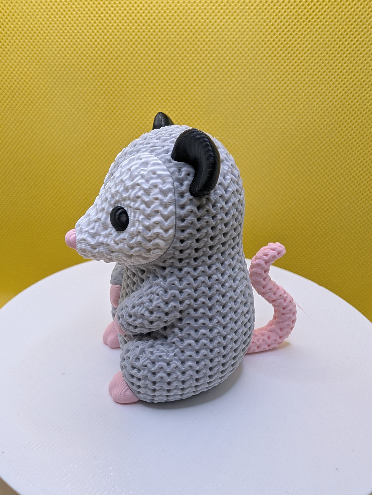 Side view of knitted-style opossum showing curved pink tail